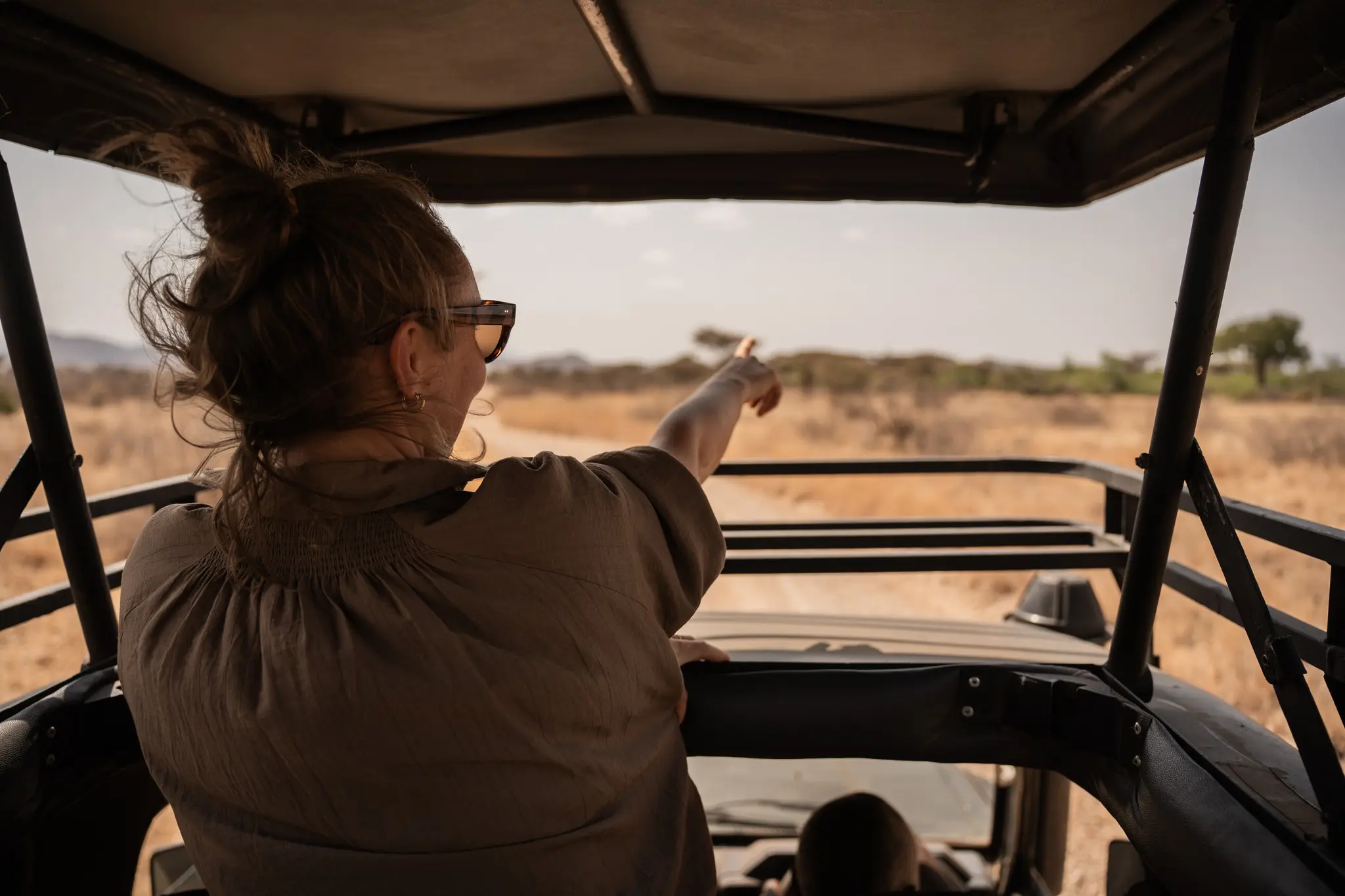 Frau, die aus einem Safari-Fahrzeug in einer trockenen Landschaft zeigt