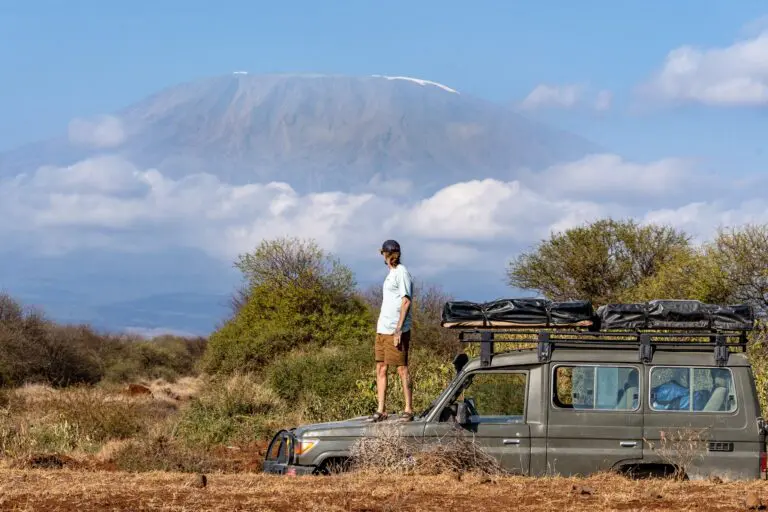 man standing on safari vehicle with mount kilimanjaro in background