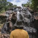 person in hat looking up at a large waterfall in Tanzania