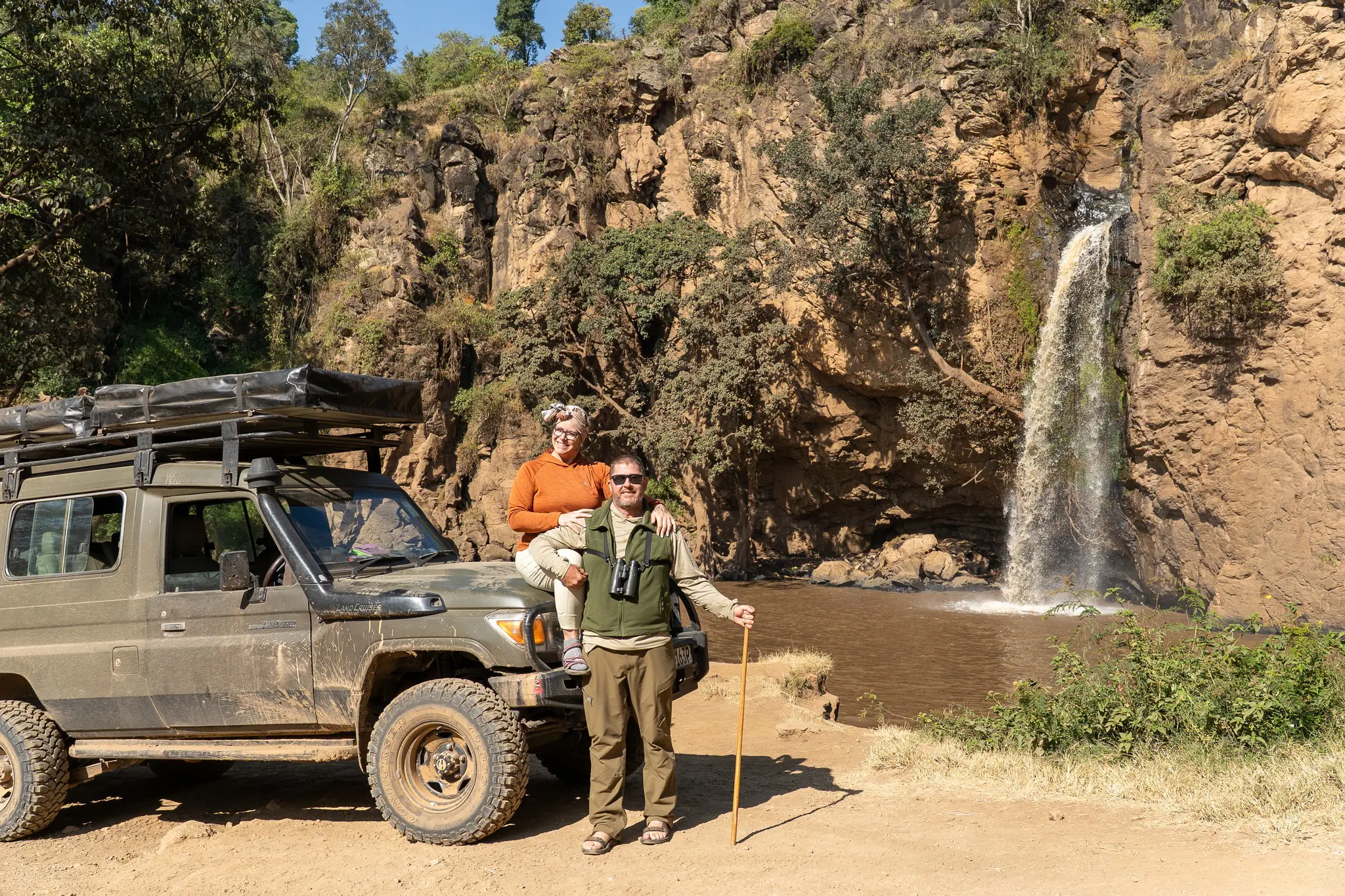 Paar mit Safarifahrzeug und Wasserfall in Afrika